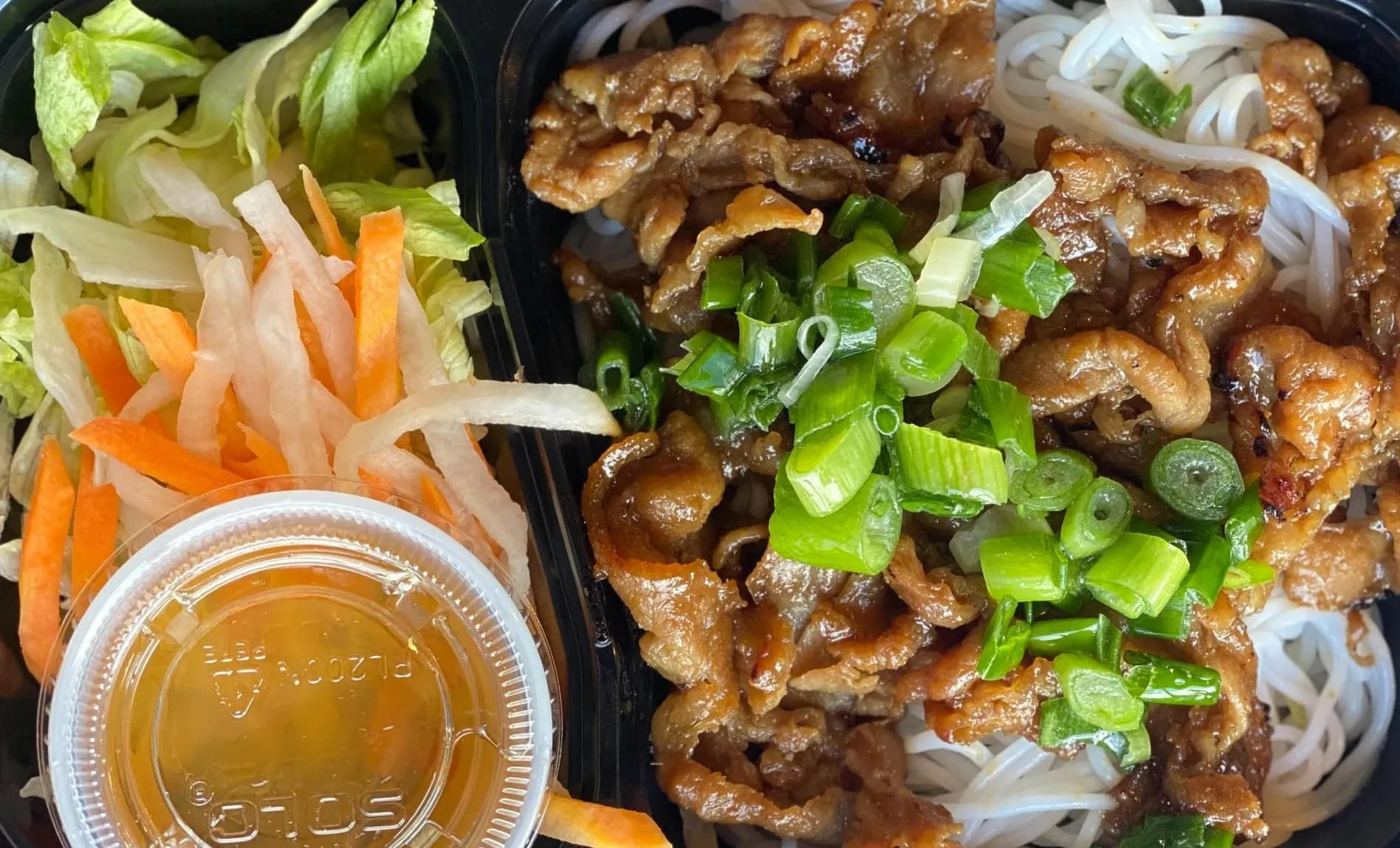 Prepared meal with noodles, vegetables, and protein in a delivery tray